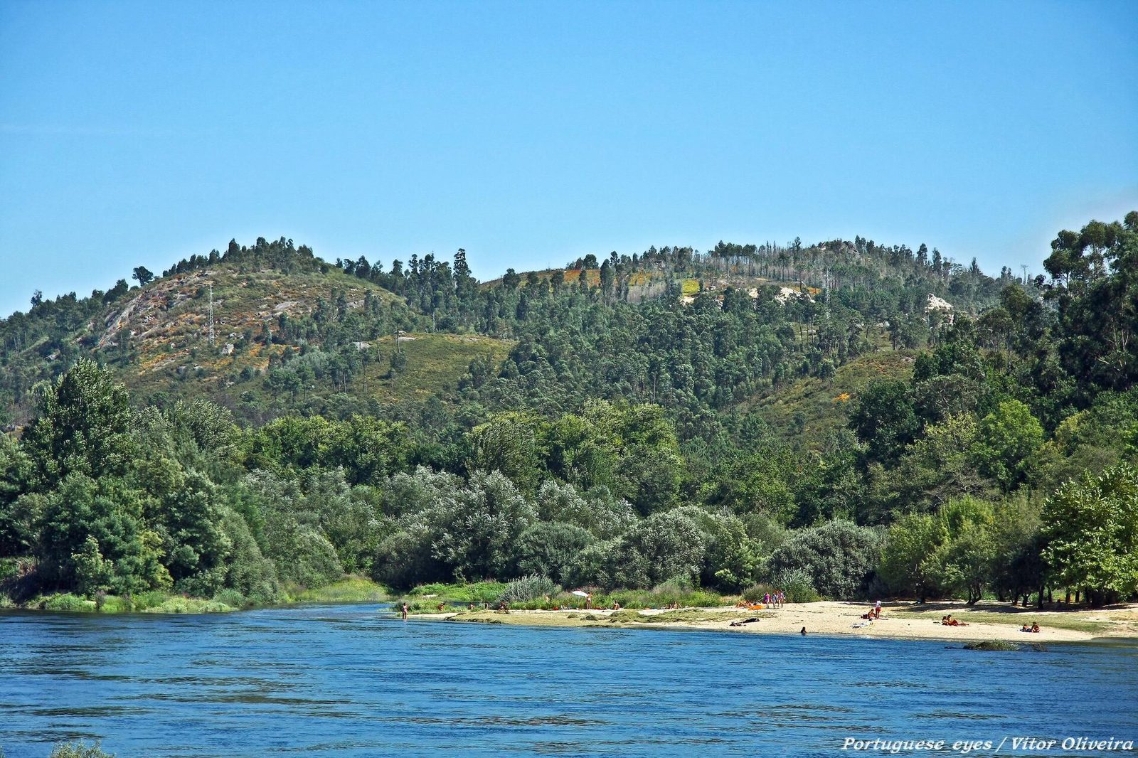 Praia fluvial no rio, com margens verdes, no Alto Minho